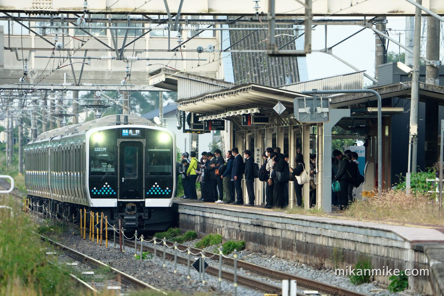 明科駅へと入ってくるE131系。ホームには大勢の乗客が待っている。